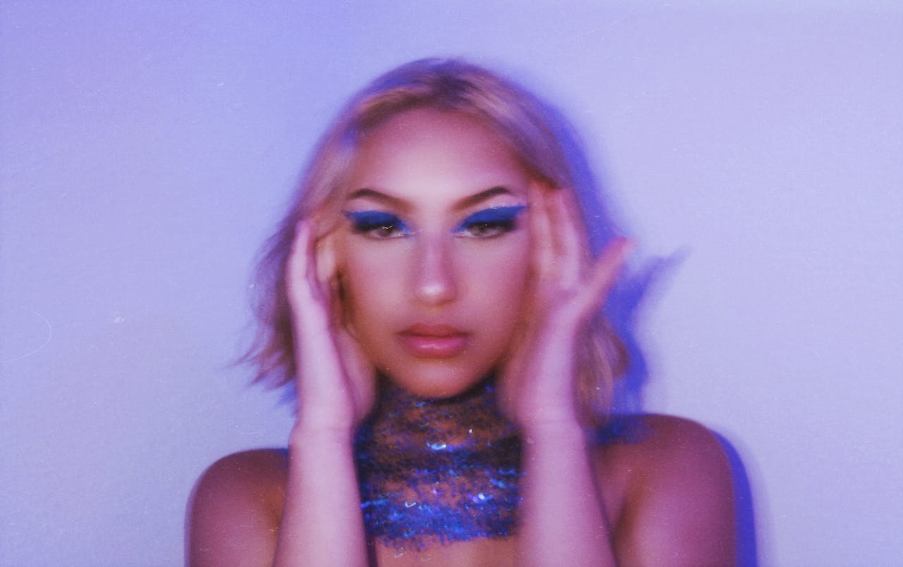 Blurred portrait of a woman with striking blue makeup and fashion-forward style.